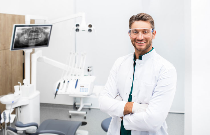 Confident-male-dentist-standing-in-his-modern-clinic